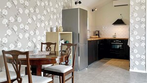 A dining area with a wooden table and chairs, a refrigerator, and a kitchen with a tiled backsplash and black appliances.