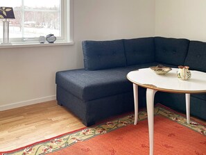 A corner seating area with a dark blue sofa, a white round table with a gold rim, and a patterned rug. - 4 Person Holiday Home in Aneby (Aneby)