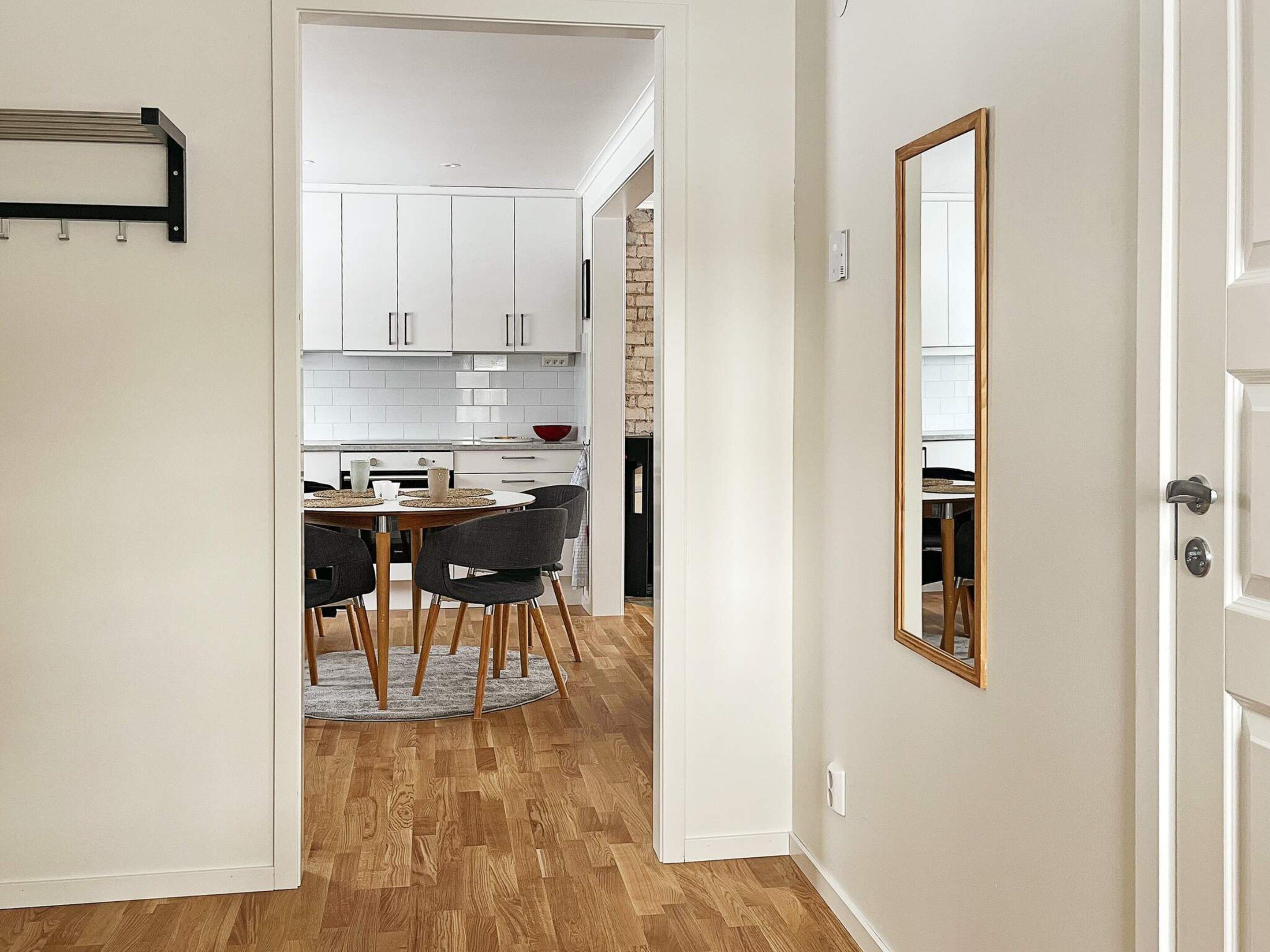 A modern kitchen with white cabinets, a dining area with a round table and chairs, and a wooden floor.