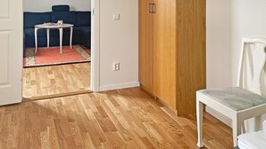 A room with a wooden floor, a white chair, a blue sofa, a small white table, and a wooden wardrobe. - 4 Person Holiday Home in Aneby (Aneby)