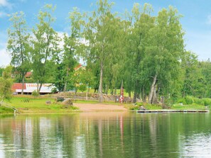 Um parque à beira de um lago, com bancos, um cais e um edifício ao fundo.