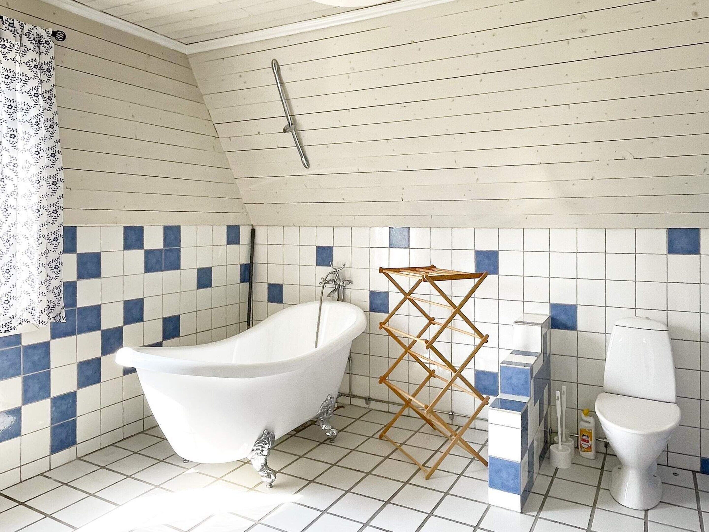 Un baño con una bañera independiente, un tendedero de madera, un inodoro y un cabezal de ducha.