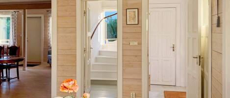 A room with a wooden floor, a dining table with chairs, a staircase, and a white door.