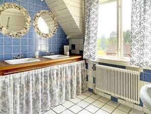 Een badkamer met twee wastafels, een raam met gordijnen, een radiator en een houten aanrecht.