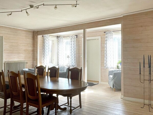 A dining room with a round table and chairs, wooden floors, and large windows with curtains. - 8 Person Holiday Home in Vetlanda (Vetlanda)