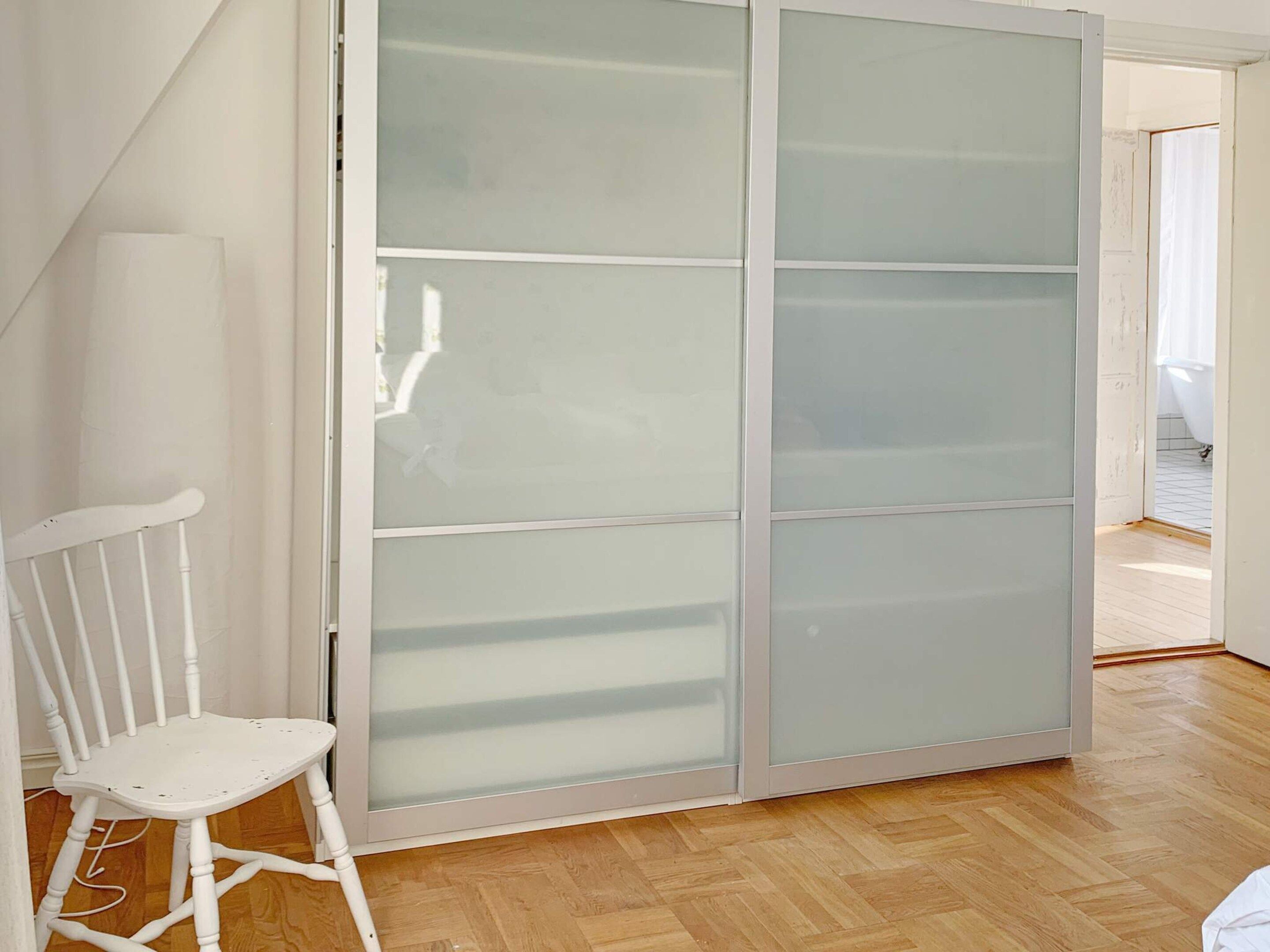 A room with a sliding glass door, a white chair, and a wooden floor.