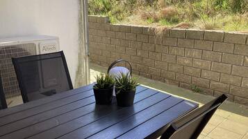 A patio area with a table and chairs, a brick wall, and a view of greenery.
