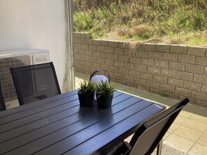 Un espace patio aménagé avec une table et des chaises, un mur en briques et une vue sur la verdure.