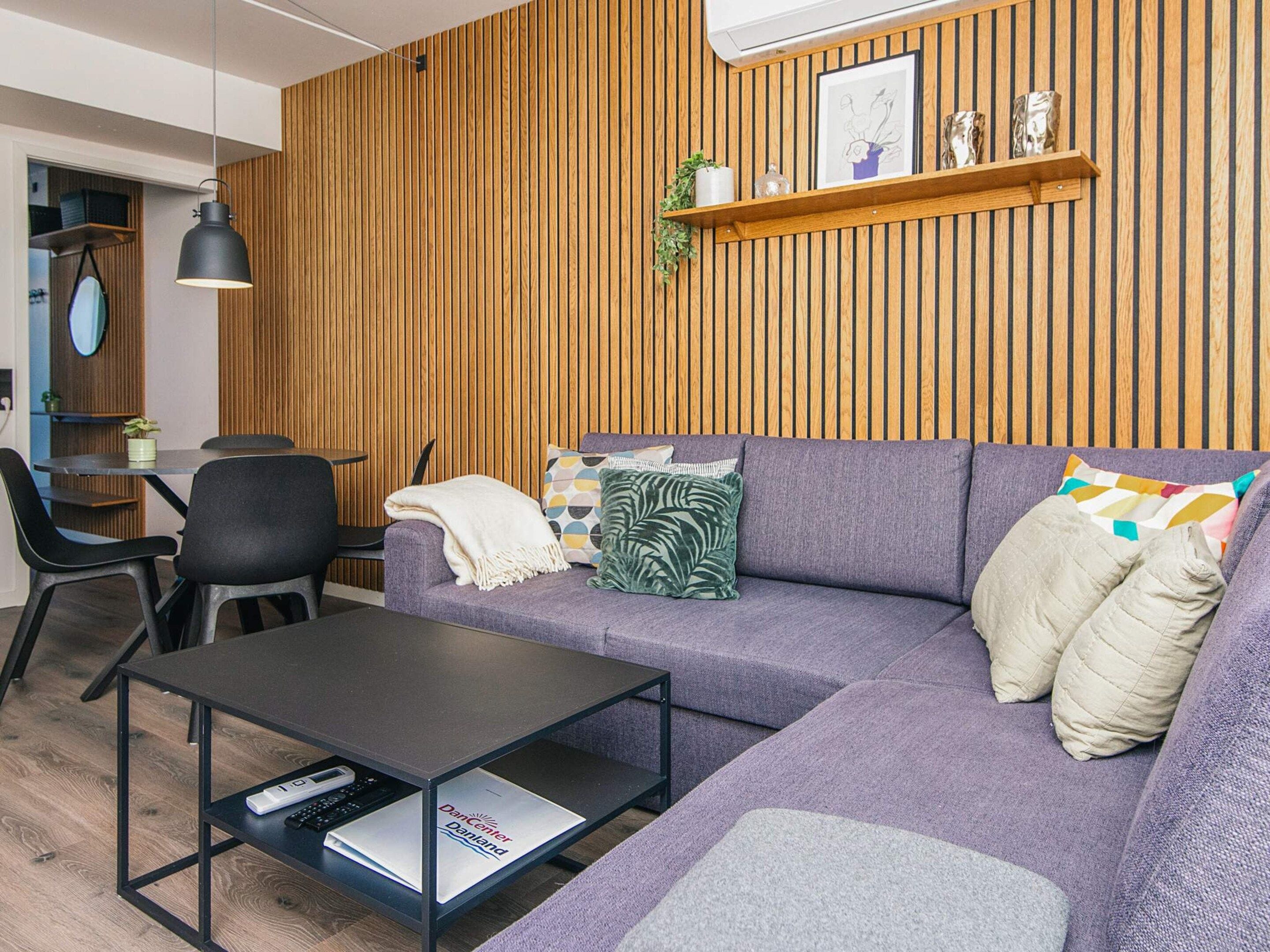 A modern living room with a wooden panel wall, a purple sofa, a black coffee table, and a small side table.