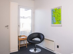 A room with a door leading to a balcony, a black chair, a small wooden table with plants, and a map on the wall. - 4 Star Holiday Home in Ringkobing (Ringkobing)
