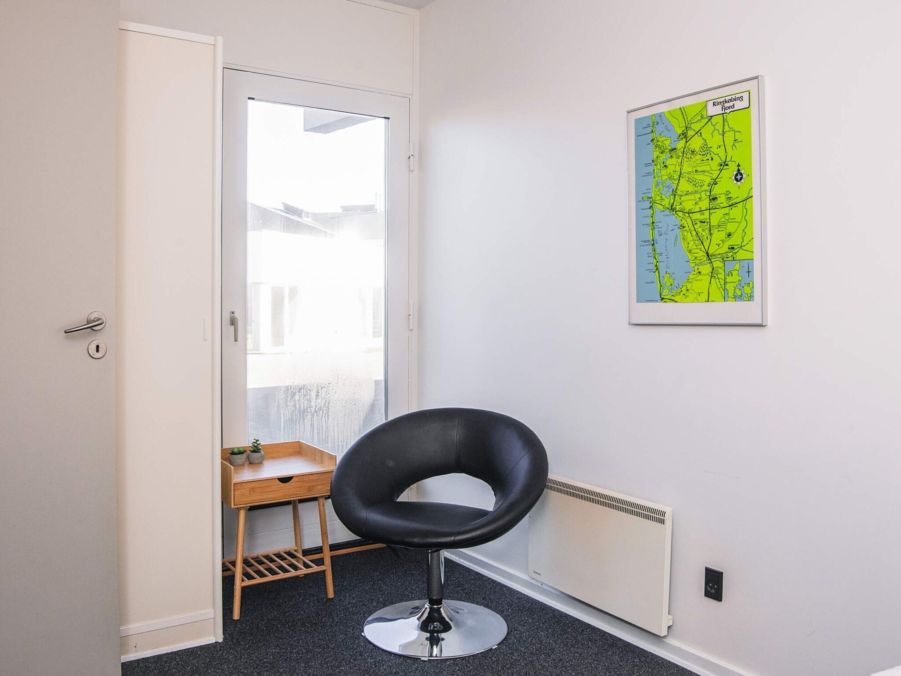 A room with a black chair, a small wooden table with two potted plants, a radiator, and a map on the wall.