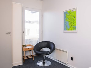 A room with a black chair, a small wooden table with two potted plants, a radiator, and a map on the wall. - 4 Star Holiday Home in Ringkobing (Ringkobing)