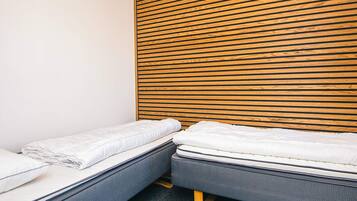 A room with two single beds, a wooden slatted headboard, and a plain white wall.