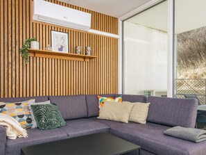 A modern living room with a sectional sofa, a coffee table, and a wooden wall panel. - 4 Star Holiday Home in Ringkobing (Ringkobing)