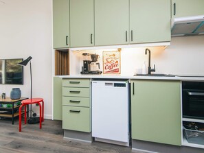 A compact kitchen with green cabinets, a coffee machine, and a dishwasher. - 4 Star Holiday Home in Ringkobing (Ringkobing)