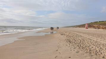 A sandy beach with footprints leading to the water, a red and white lifeguard tower, and a grassy hill in the background.