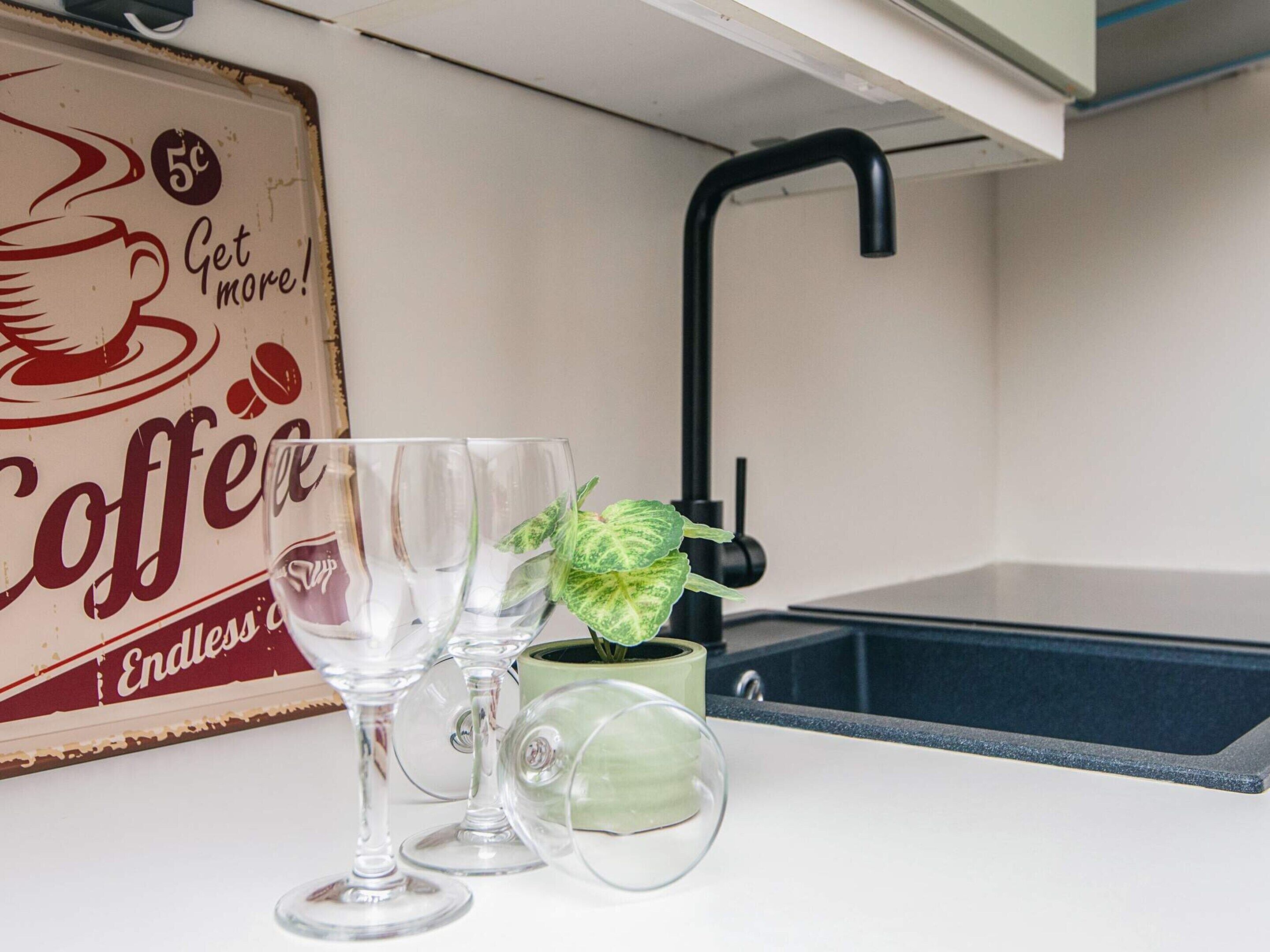 Uma cozinha com um letreiro de café vintage, uma pia e três copos de vinho.