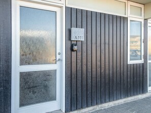 A building facade with a dark wooden panel exterior, a white door with a glass panel, and a mailbox with a house number plaque. - 4 Star Holiday Home in Ringkobing (Ringkobing)