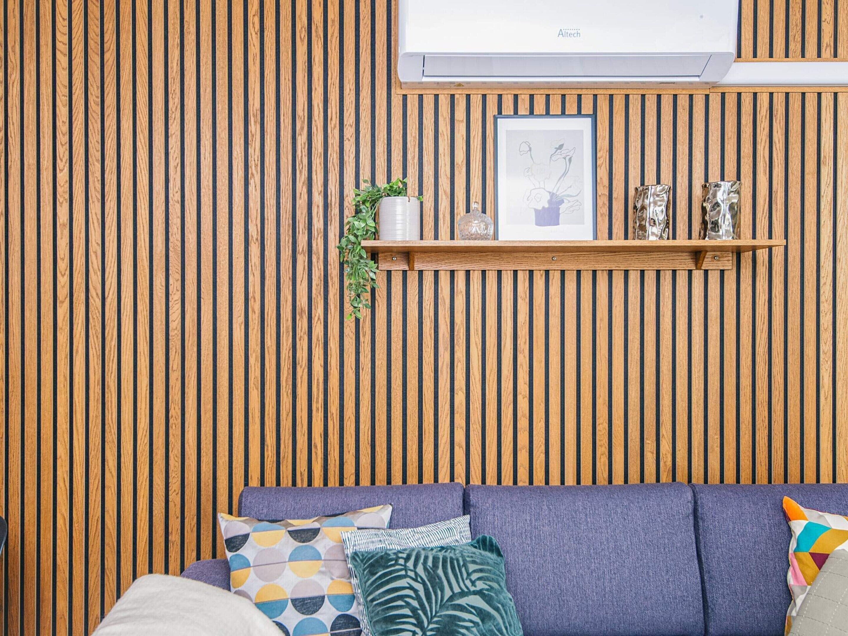 Un soggiorno con parete in listelli di legno, condizionatore a muro, una mensola con oggetti decorativi e un divano con cuscini.