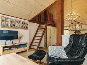 A living room with a TV, wooden entertainment unit, a black leather sofa, a candelabra, and a wooden staircase. - 6 Person Holiday Home in Nykobing M (Nykobing Mors)