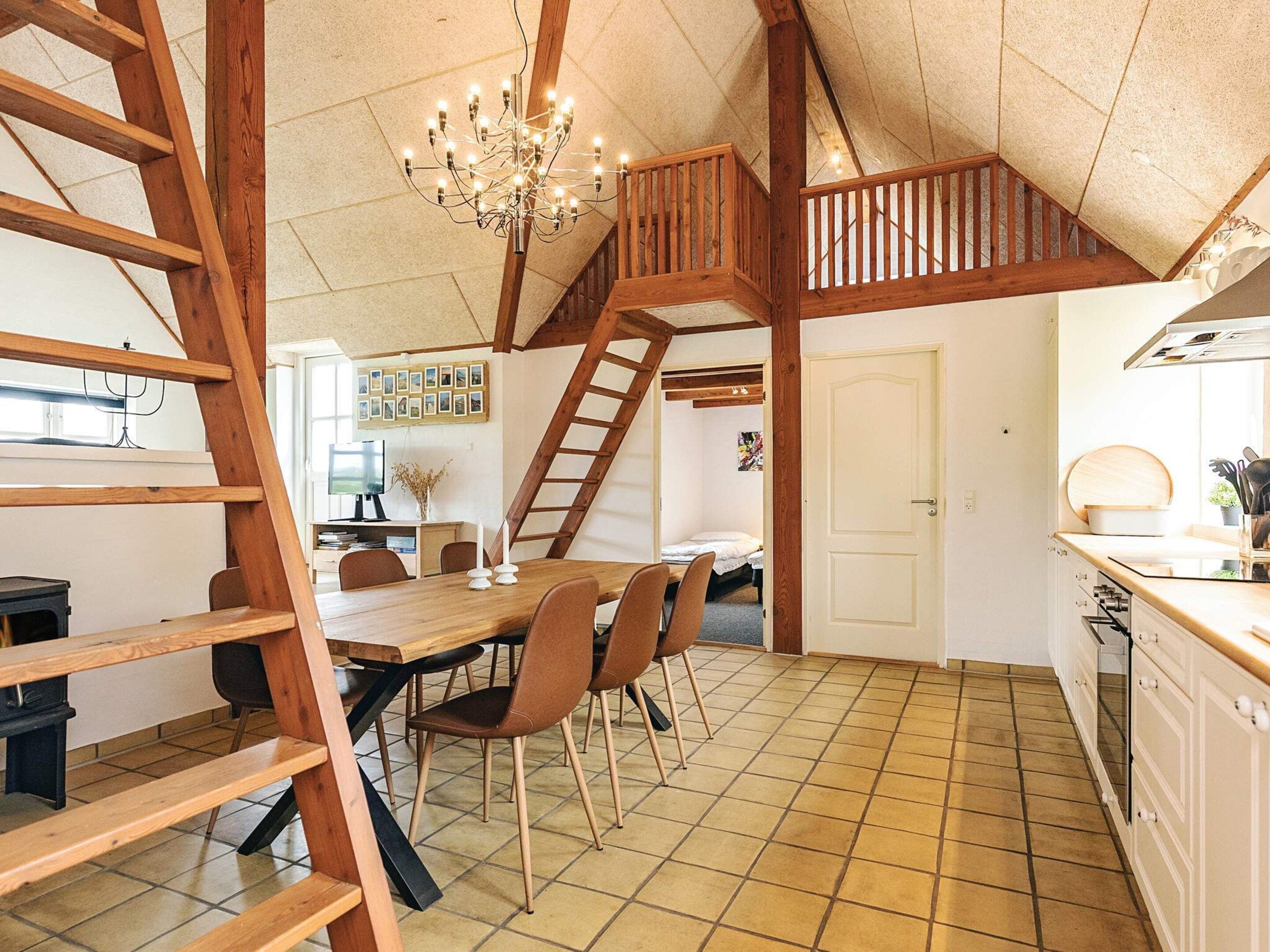 A spacious kitchen with a wooden staircase, a dining area with chairs, and a chandelier.