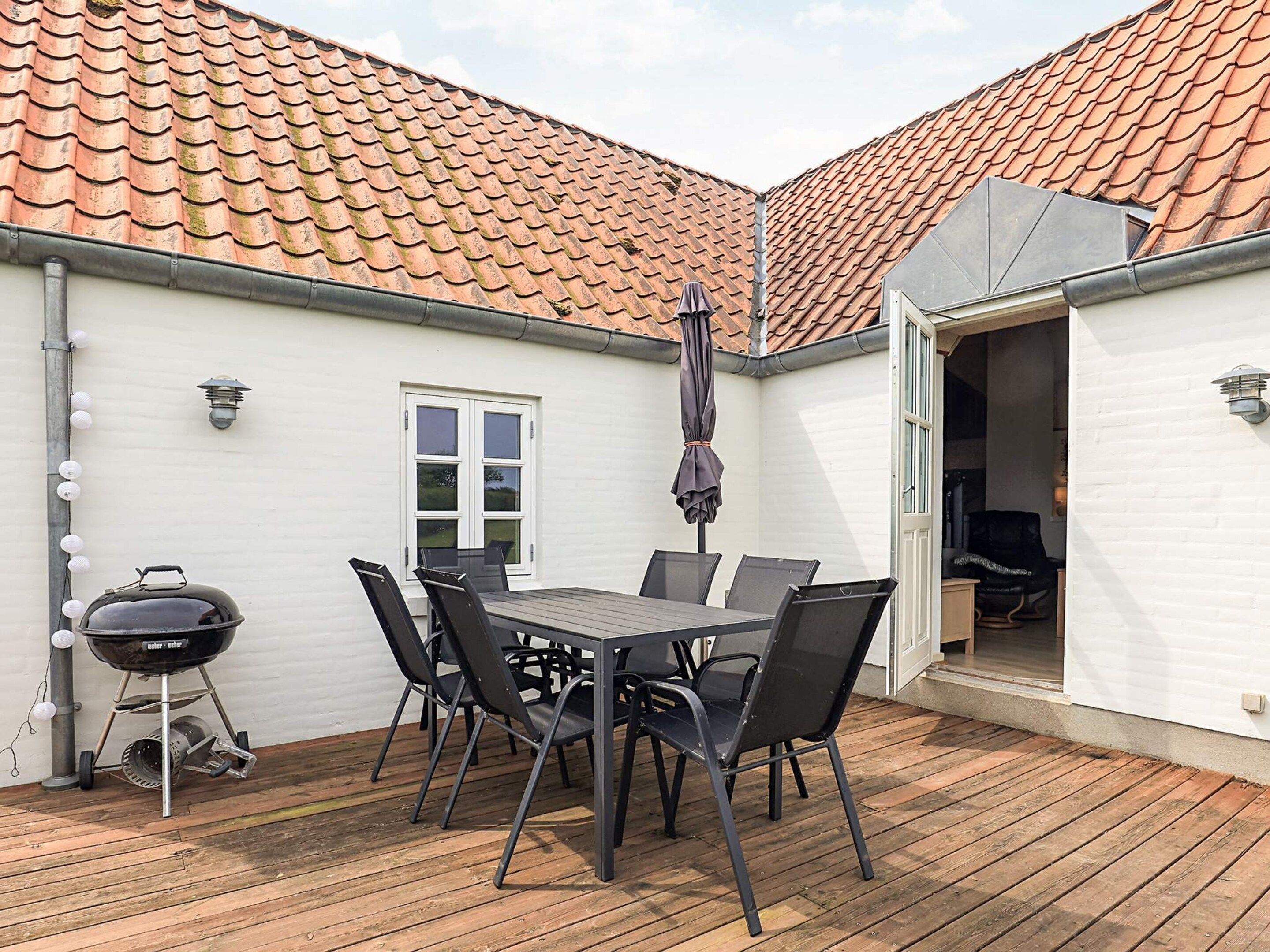A patio with a table and chairs, a barbecue grill, and a white building with a tiled roof.