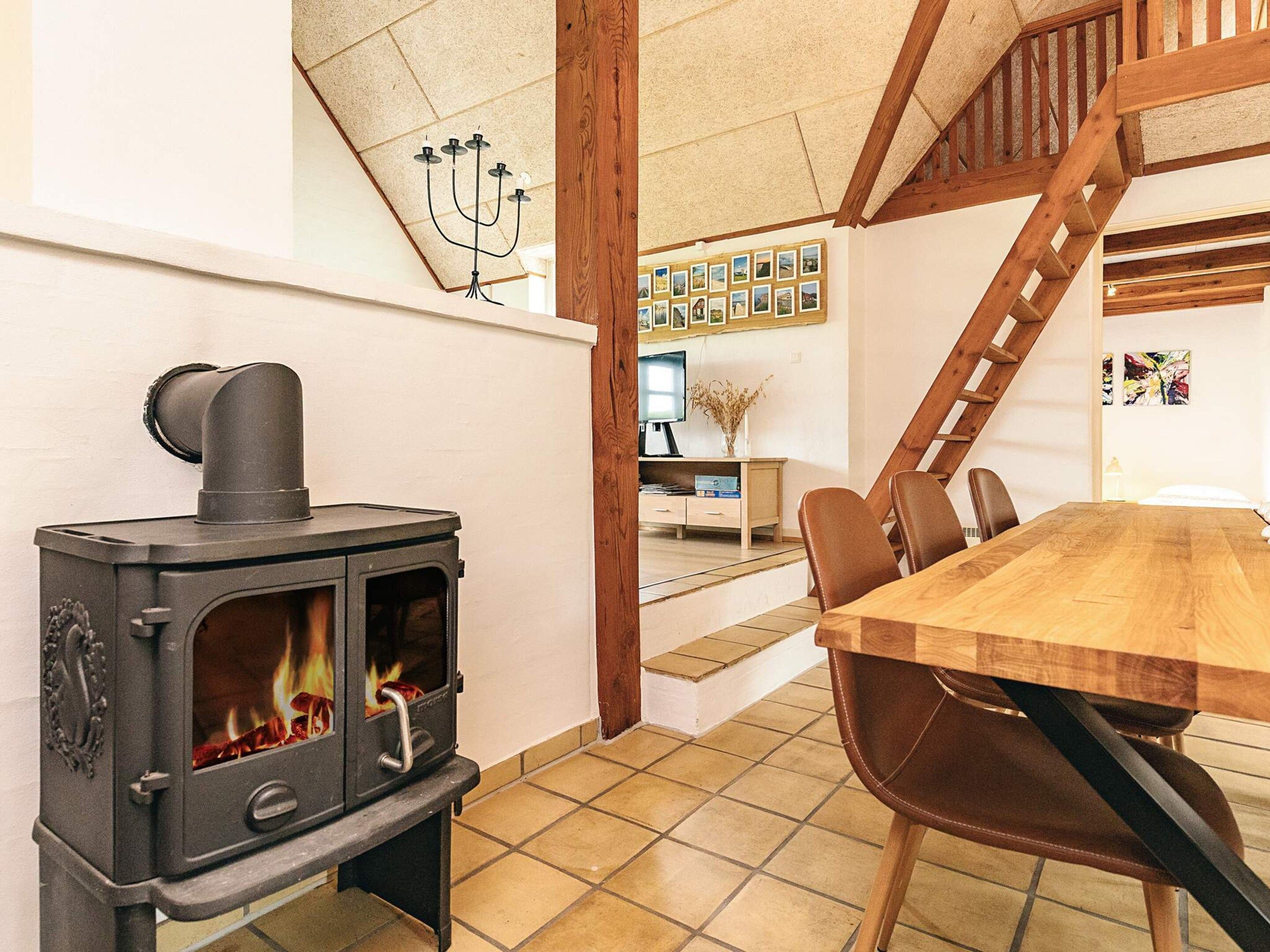Une pièce avec un poêle à bois, une table à manger avec des chaises, un escalier et un mur orné de tableaux.