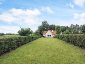A white building with a red roof, surrounded by a neatly trimmed hedge and a grassy lawn. - 6 Person Holiday Home in Nykobing M (Nykobing Mors)