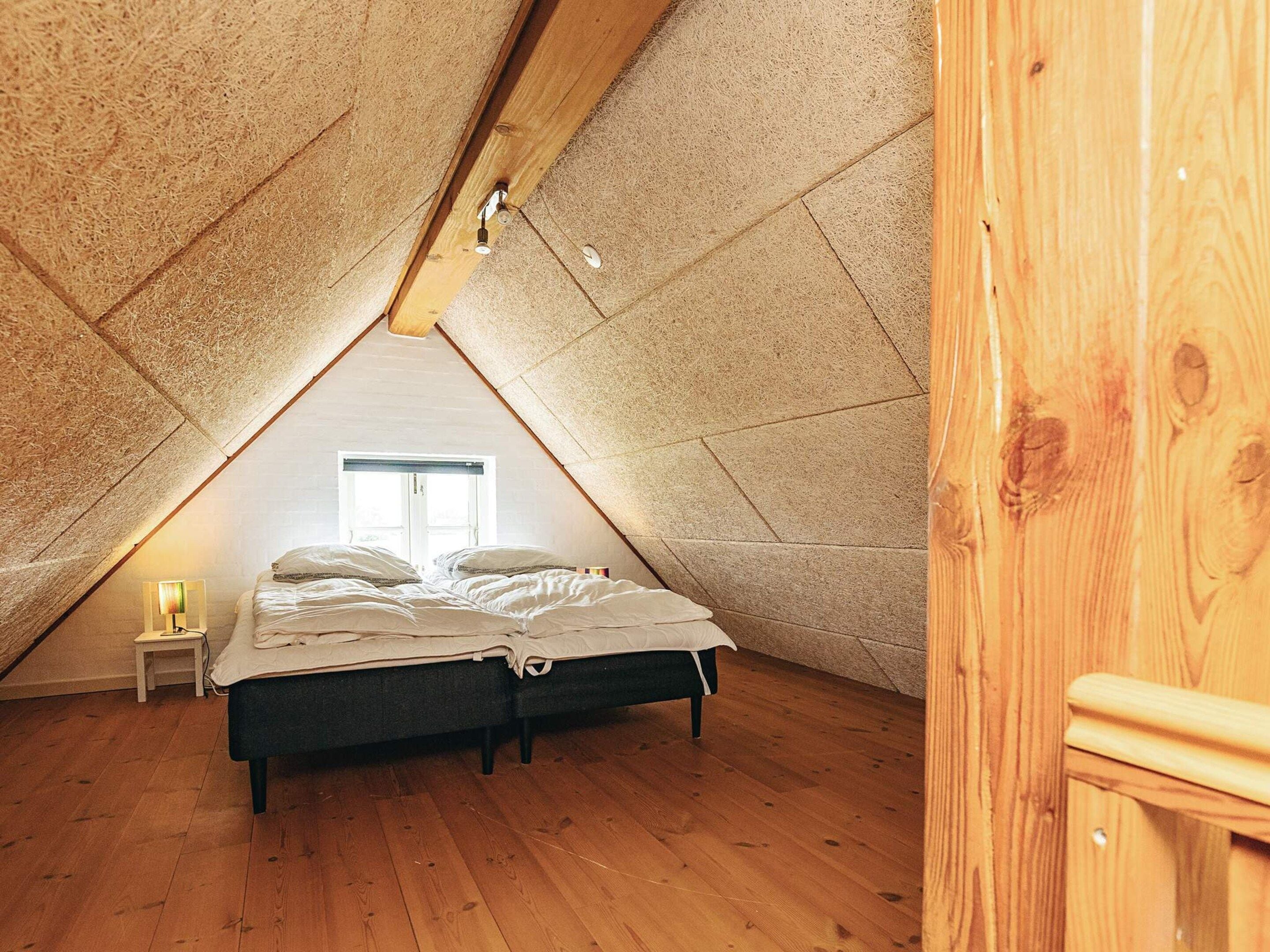 A bedroom with a sloped ceiling, a bed, a bedside table, and a window.