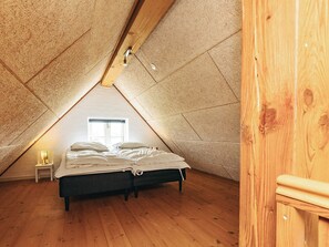 Un dormitorio con techo inclinado, una cama, una mesita de noche y una ventana.