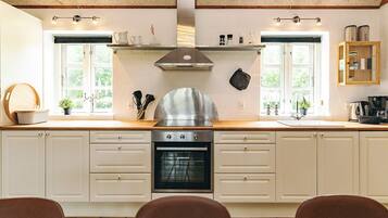 A kitchen with a stove, oven, and a range hood. There are two windows with curtains, a sink, and a countertop with various items.