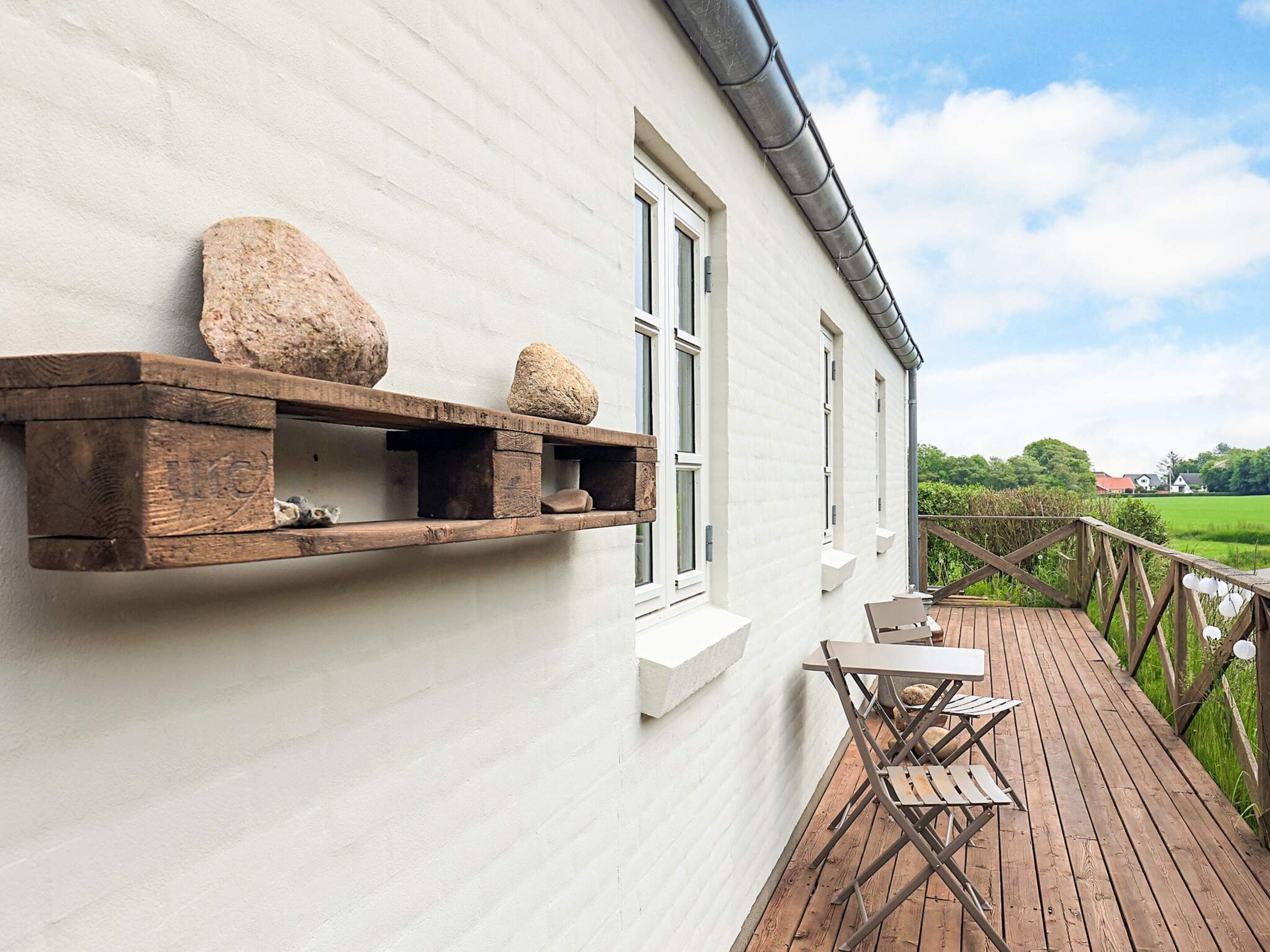 A white building with a wooden deck, a table and chairs, and a stone shelf.