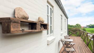 A white building with a wooden deck, a table and chairs, and a stone shelf.