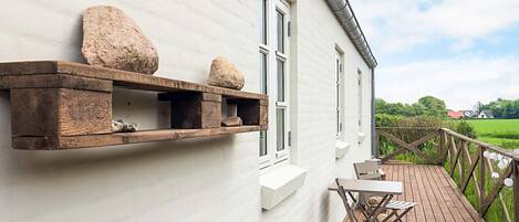 Un edificio blanco con terraza de madera, una mesa y sillas, y una estantería de piedra.