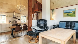 Amplia sala de estar con una mesa de comedor, un sillón de cuero negro, una mesa de centro de madera y un sofá con cojines azules.