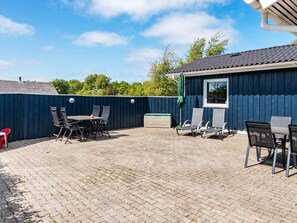 A patio area with a table and chairs, a covered seating area, and a blue building with a window. - 6 Person Holiday Home in Hemmet (Hemmet)