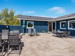 A covered outdoor seating area with tables and chairs, a blue building with windows, and a paved ground. - 6 Person Holiday Home in Hemmet (Hemmet)
