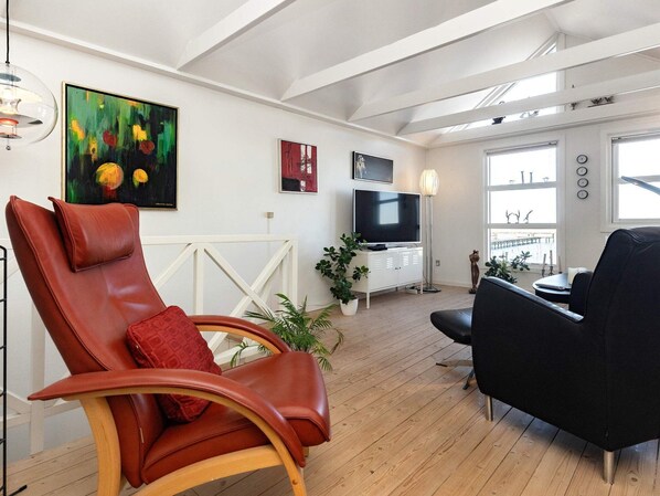 A modern living room with a leather armchair, a black sofa, a TV, and artwork on the walls.