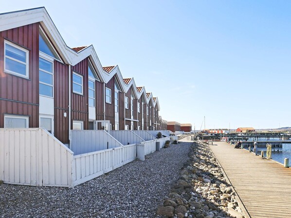 A row of modern, multi-story buildings with a wooden facade and white trim, adjacent to a wooden dock extending into a marina. - 5 Person Holiday Home in Nibe (Nibe)