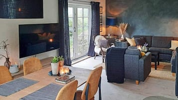 Una sala de estar moderna con un sofá, una mesa de comedor con sillas, un televisor y un ventanal con cortinas.