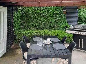 An outdoor patio with a table and chairs, a grill, and a green ivy-covered wall. - 6 Person Holiday Home in Bindslev (Bindslev)