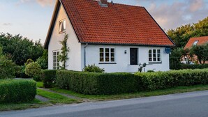 Une maison à deux étages, avec un toit recouvert de tuiles rouges, des murs blancs et une cheminée.