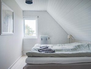 Une chambre avec un plafond en pente, un radiateur, une fenêtre et un lit avec une couverture.