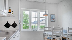 A kitchen with white cabinetry, a window with a view, and a dining area with chairs and a table. - 6 Person Holiday Home in Bindslev (Bindslev)