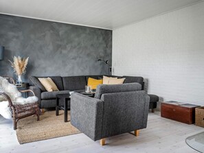 A modern living room with a grey sofa, a wooden coffee table, and a wicker chair. - 6 Person Holiday Home in Bindslev (Bindslev)
