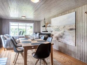 Un coin repas avec une table en bois, des chaises et un grand tableau représentant une scène de plage.