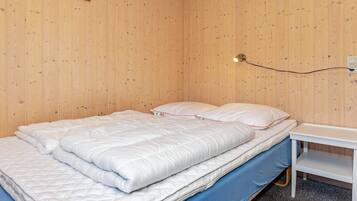 A single bed with a white duvet and pillows, a bedside table, and a wall-mounted light fixture.
