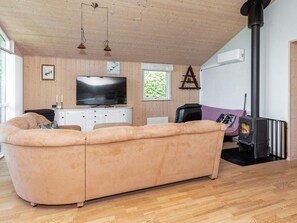 Un salon chaleureux avec un grand canapé beige, un téléviseur à écran plat, des murs lambrissés, une cheminée et une fenêtre donnant sur un paysage verdoyant.