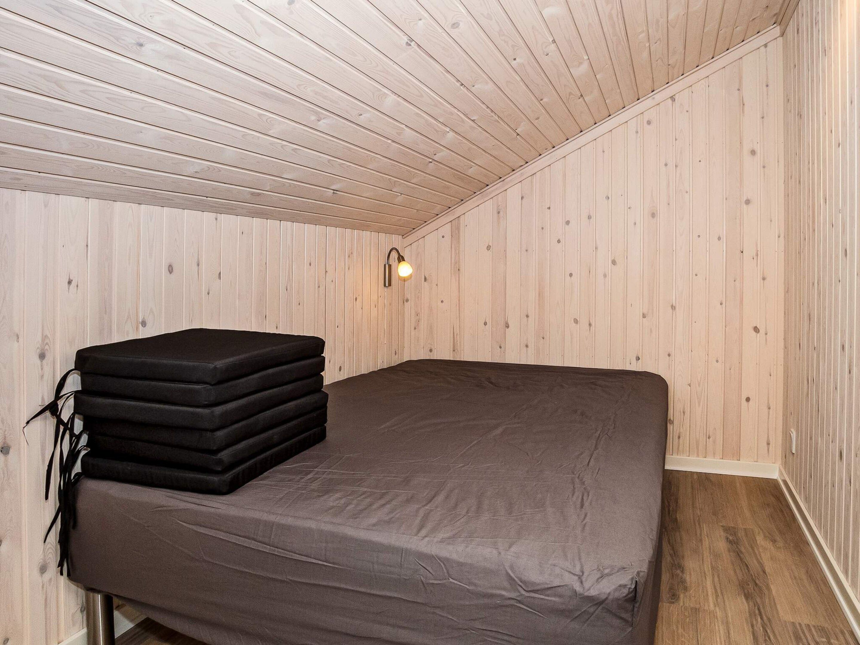 A small, single-bed room with wooden walls and a sloped ceiling.