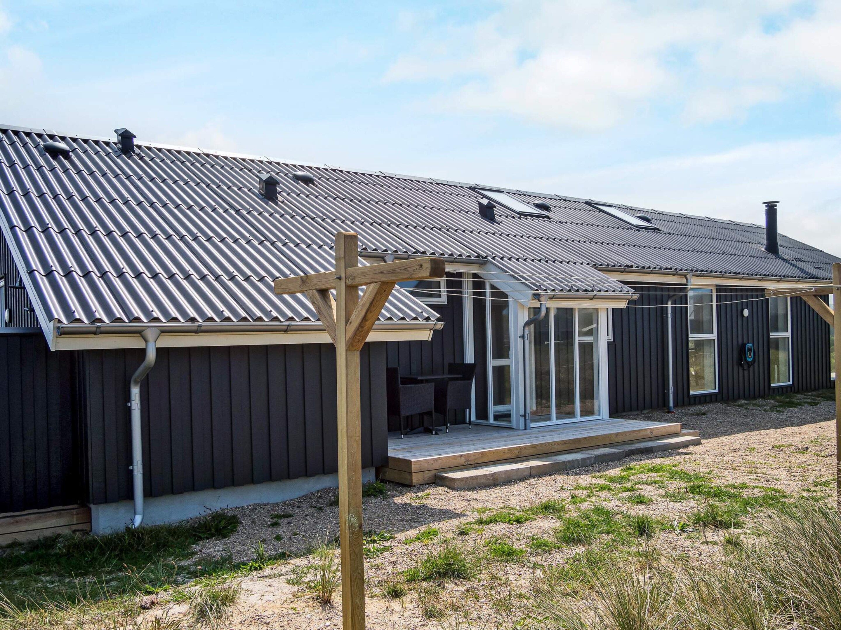 Une maison moderne avec un toit en métal, une pergola en bois et un espace de détente extérieur abrité.